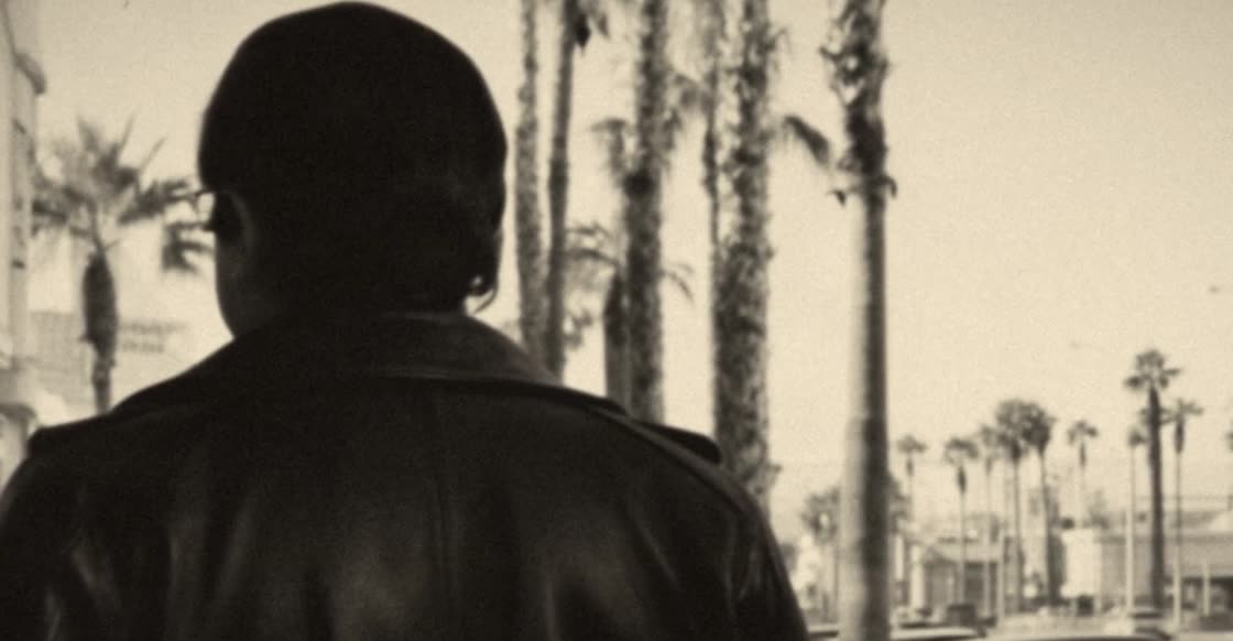 Fotograma en blanco y negro de un hombre de espaldas frente a una calle con palmeras